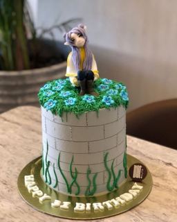 White brick-wall cake with green grass and girl topper, by DOT Cake Art