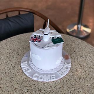 White cake with plane and flags, welcome back, by DOT Cake Art