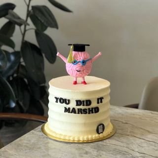 White cake with a brain character in a grad cap, by DOT Cake Art