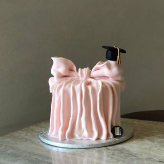 Pink cake with a large bow and graduation cap, by DOT Cake Art