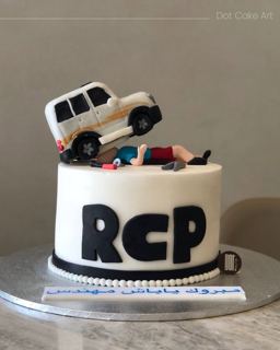 White cake with an SUV and figure on top, by DOT Cake Art