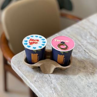 Two cup cakes in blue and pink with ring and hearts, by DOT Cake Art