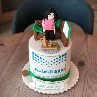 كيكة بيضاء بمجسم معلمة على كنبة ودلة وشعار وزارة التعليم وتهنئة تقاعد من دوت كيك آرت