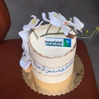 كيكة بيضاء بأوركيد أبيض وشعار أرامكو السعودية وتهنئة ترقية من دوت كيك آرت