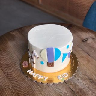 كيكة بيضاء بمنطاد وحصان منقط ونجوم زرقاء بعبارة Happy Eid من دوت كيك آرت