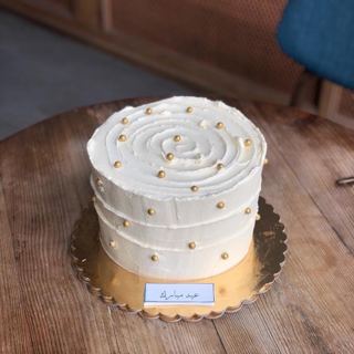 كيكة بيضاء بخطوط كريمة حلزونية ولؤلؤ ذهبي بثيم عيد مبارك من دوت كيك آرت