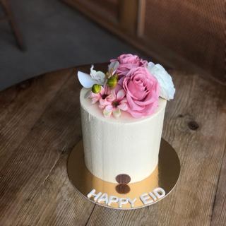 كيكة بيضاء بورود وردية وزهور صغيرة بعبارة Happy Eid من دوت كيك آرت