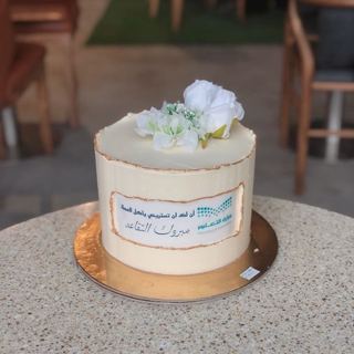 White cake with white flowers and an organisation logo, by DOT Cake Art