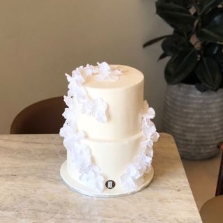 Two-tier white cake with white flowers, by DOT Cake Art