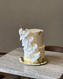 Two-tier beige cake with white orchids, by DOT Cake Art