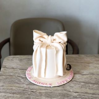 White cake wrapped with a large bow, by DOT Cake Art